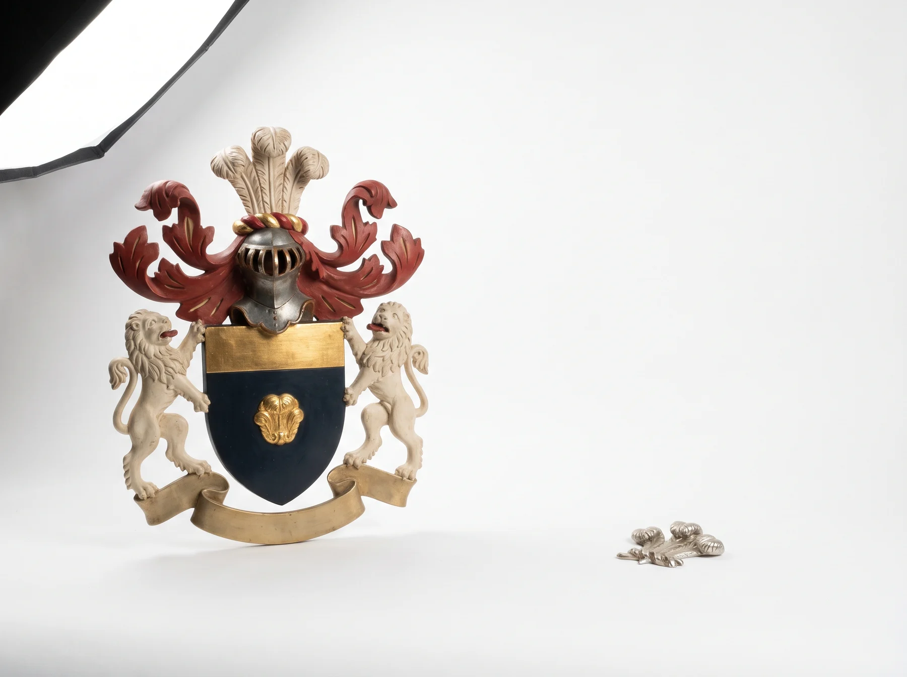 A full heraldic achievement panel beside the crest on its own, cast as a coin-sized silver badge, both shown at true relative scale