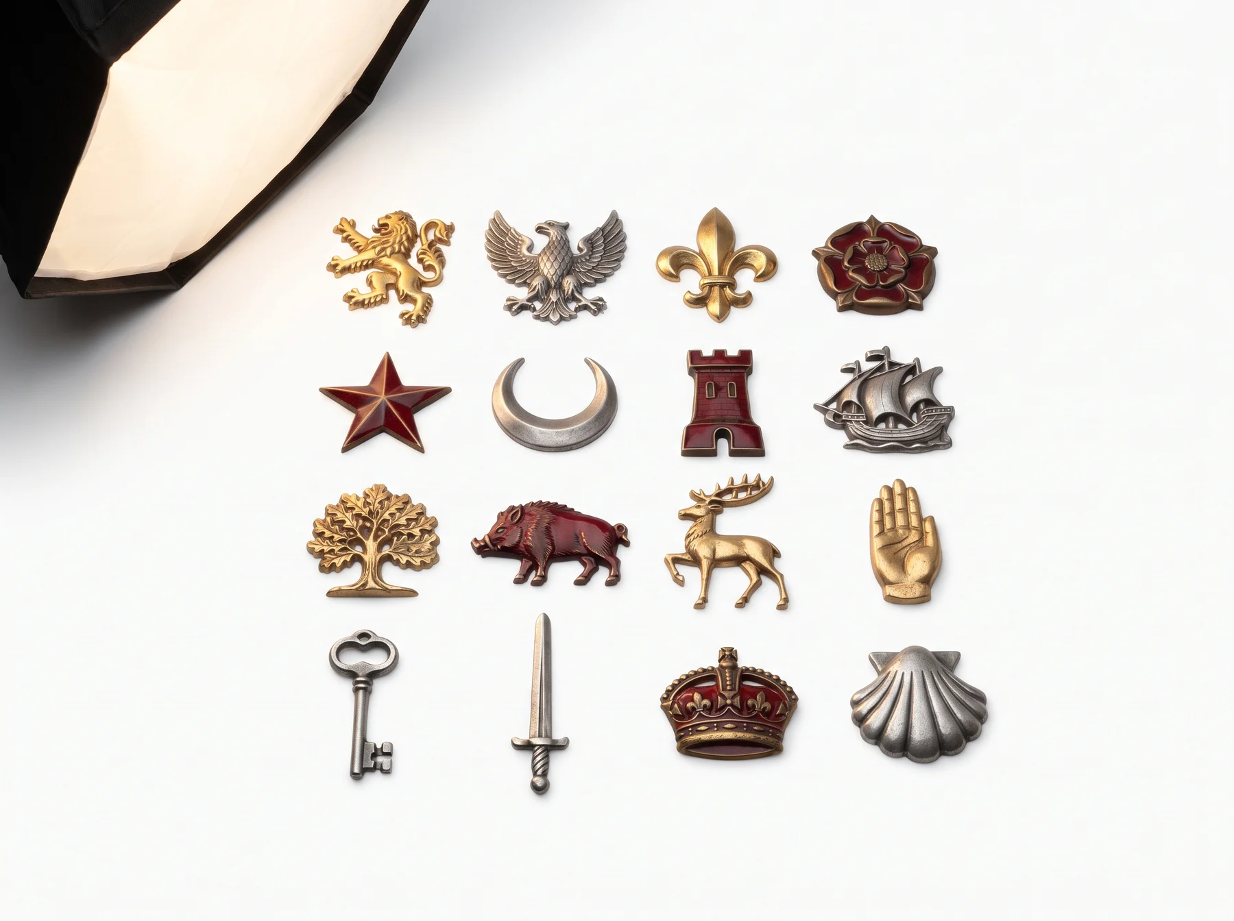 Sixteen cast metal heraldic charges laid out in a grid: lion, eagle, fleur-de-lis, rose, mullet, crescent, tower, ship, oak, boar, stag, hand, key, sword, crown and scallop shell
